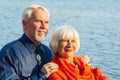 Cheerful senior citizens woman and man are standing and hugging on the lake, against the background of the bridge Royalty Free Stock Photo