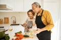 Cheerful senior couple cooking and using digital tablet, looking for nice recipe on Internet in kitchen at home Royalty Free Stock Photo