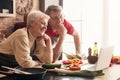 Cheerful Senior Couple Using Laptop In Kitchen, Watching Culinary Recipies Together