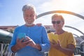Cheerful senior couple walking on a bridge in the city. Looking at their own mobile phone and smiling. Elderly modern and