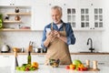 Cheerful senior man in apron using smartphone while cooking in kitchen Royalty Free Stock Photo