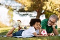 Cheerful senior man with beard and black little boy lie on plaid with ball, rest in park, outdoor Royalty Free Stock Photo