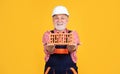 cheerful senior man bricklayer in hard hat on yellow background