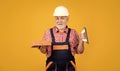 cheerful senior man bricklayer in helmet on yellow background