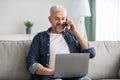 Cheerful senior man talking on phone and using laptop Royalty Free Stock Photo