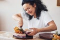 Cheerful senior woman with black curly hair making slices of fresh dietical cake on the kitchen