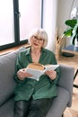 Cheerful senior woman sitting on the couch reading a book at home. Royalty Free Stock Photo