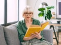 Cheerful senior woman sitting on the couch reading a book at home. Royalty Free Stock Photo