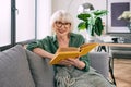 Cheerful senior woman sitting on the couch reading a book at home. Royalty Free Stock Photo