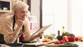 Cheerful senior woman using digital tablet at kitchen, reading news Royalty Free Stock Photo