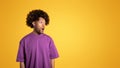 Cheerful shocked black adult curly man in purple t-shirt with open mouth looks at empty space
