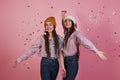 Cheerful sisters. New year conception. Two twins playing throwing golden confetti in the air in the studio with pink Royalty Free Stock Photo