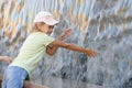 Cheerful six year girl in summer clothes hand trying to get the water artificial waterfall