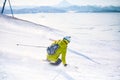 Cheerful skier girl in green jacket in front of snowy mountains