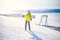 Cheerful skier girl in green jacket in front of snowy mountains