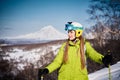 Cheerful skier girl in green jacket in front of snowy volcano