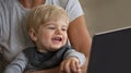 Cheerful small child laughing at someting on a computer screen while sitting on motherÃ¢â¬â¢s lap.