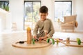 Cheerful small european boy in pajamas sits on floor plays with road and cars, enjoy spare time in nursery room