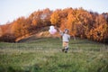 Cheerful small girl with balloons running in autumn nature.