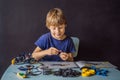 Cheerful smart schoolboy sitting at the table and constructing a robotic device at home