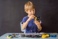 Cheerful smart schoolboy sitting at the table and constructing a robotic device at home