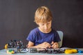 Cheerful smart schoolboy sitting at the table and constructing a robotic device at home