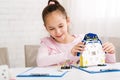 Cheerful smart schoolgirl constructing robotic device at lesson