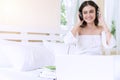 Cheerful smile woman listening music with headphones, book and laptop feeling relax sitting on white bed in the morning.