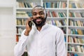 Cheerful smiling African male student or businessman, wearing white shirt, talking on the phone, standing in modern Royalty Free Stock Photo