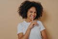 Cheerful smiling afro girl showing shhh sign, keep silence gesture, with index finger near lips