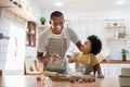 Cheerful smiling Black son enjoying playing with his father while doing bakery at home. Playful African family having fun cooking