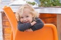 Cheerful smiling blonde little girl sitting on orange chair in cafe outside Royalty Free Stock Photo