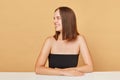 Cheerful smiling brown haired woman wearing black top posing isolated over beige background looking away at copy space for Royalty Free Stock Photo