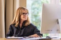 Cheerful smiling businesswoman sittint at desk and using computer for work