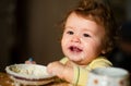 Cheerful smiling child child eats itself with a spoon Baby eating with dirty face. Smiling little child eating food on Royalty Free Stock Photo