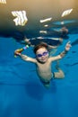 A cheerful, smiling child, a little boy, is swimming underwater in the pool. He holds sports toys in his hands and looks Royalty Free Stock Photo