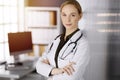 Cheerful smiling female doctor standing in sunny clinic. Portrait of friendly physician woman. Perfect medical service