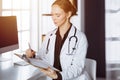 Cheerful smiling female doctor using clipboard in clinic. Portrait of friendly physician woman at work place. Medicine