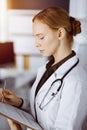 Cheerful smiling female doctor using clipboard in sunny clinic. Portrait of friendly physician woman at work. Medicine