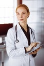 Cheerful smiling female doctor using tablet computer in sunny clinic. Portrait of friendly physician woman at work