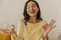 Cheerful smiling girl with closed eyes in yellow blouse stands on white background with cup of tea. Royalty Free Stock Photo