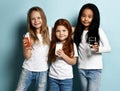 Cheerful smiling kids girls friends in blue jeans and white t-shirts stand holding glasses of water, milk and juice