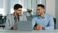 Cheerful smiling male colleagues employees cooperating in office talking working together at workplace, optimistic