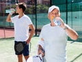 Mature man and young man drink water on padel court