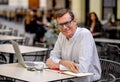 Happy attractive stylish mature man working on laptop while having coffee in outside coffee shop Royalty Free Stock Photo