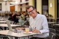 Cheerful smiling old man working on computer while having coffee in terrace coffee shop city outdoors in seniors using modern Royalty Free Stock Photo