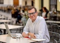 Cheerful smiling old man working on computer while having coffee in terrace coffee shop city outdoors in seniors using modern Royalty Free Stock Photo