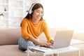 Cheerful young asian woman using laptop and headphones at home Royalty Free Stock Photo