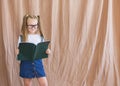 Cheerful smiling schoolboy girl returning to school reads a book on studio background. Empty space Royalty Free Stock Photo