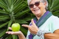 Cheerful and smiling senior woman with scarf and sunglasses holding in the hand a green apple.  Concept of healthy eating and diet Royalty Free Stock Photo